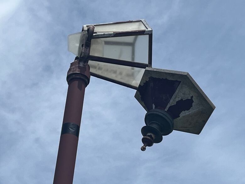 A close up of a street light, snapped in two, with the top half hanging in the wind.