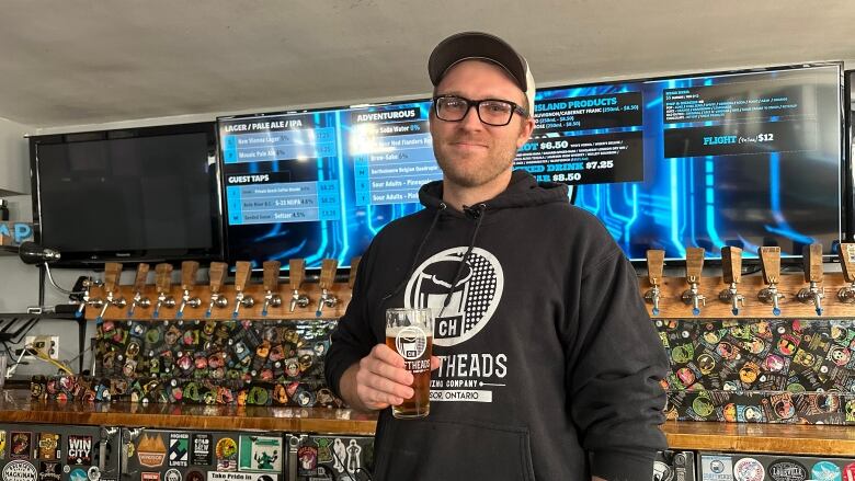 A man stands in a bar holding a beer.