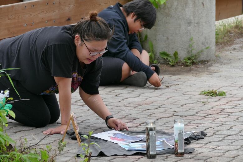 A woman crying kneels on the ground before candles and pictures.