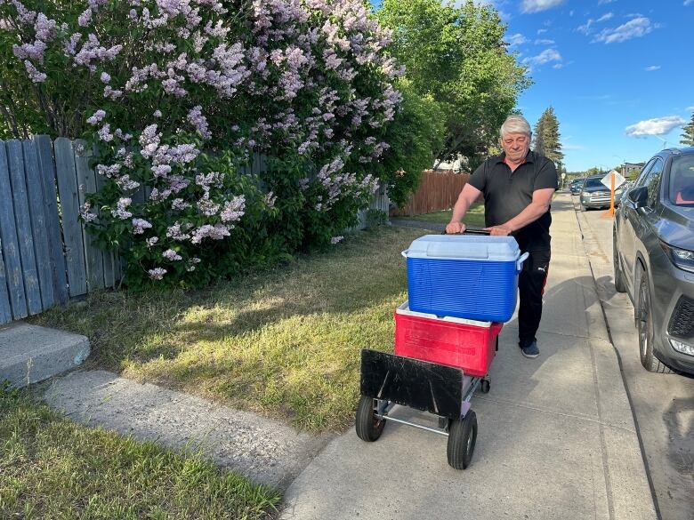 A man pushes a dolly with two coolers on top of it. 