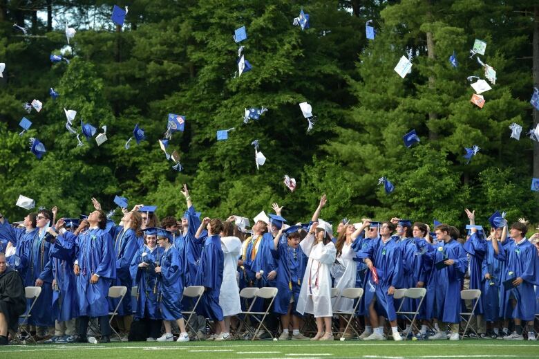 Several students are shown throwing graduation caps in the air from a distance on a grass field.