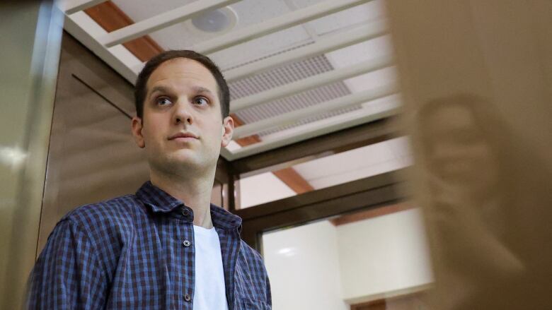 A man in a blue button-down shirt stands inside an enclosure for defendants before a court hearing.