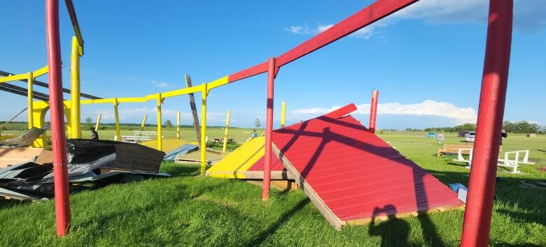 The frame of a red and yellow structure shows damage, with large platforms and metal sheets piled up on the ground.