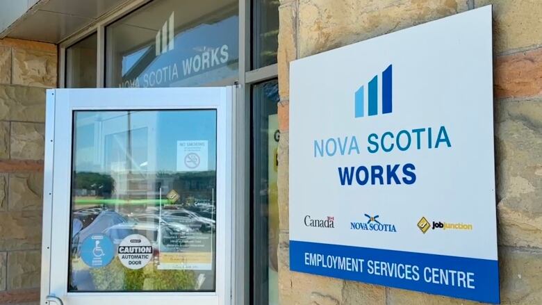 A person walks through the entry door to an office with a sign on the outer wall that says 