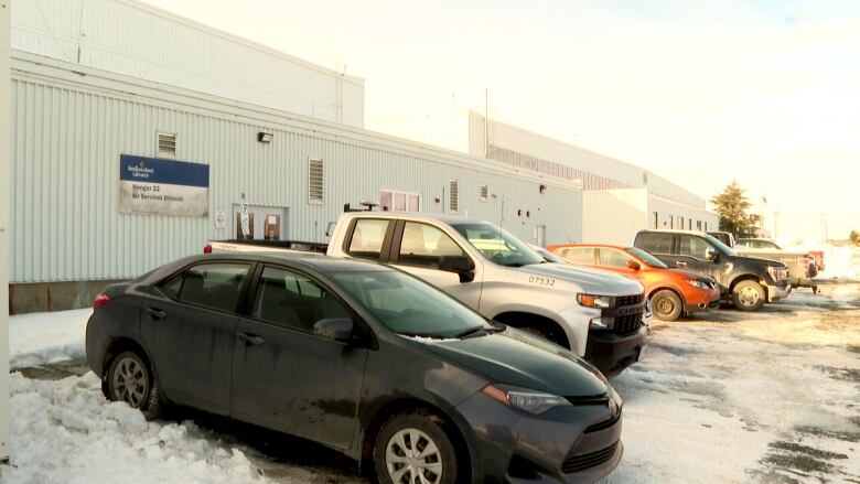 Vehicles are parked outside a large white building with a blue sign on the side