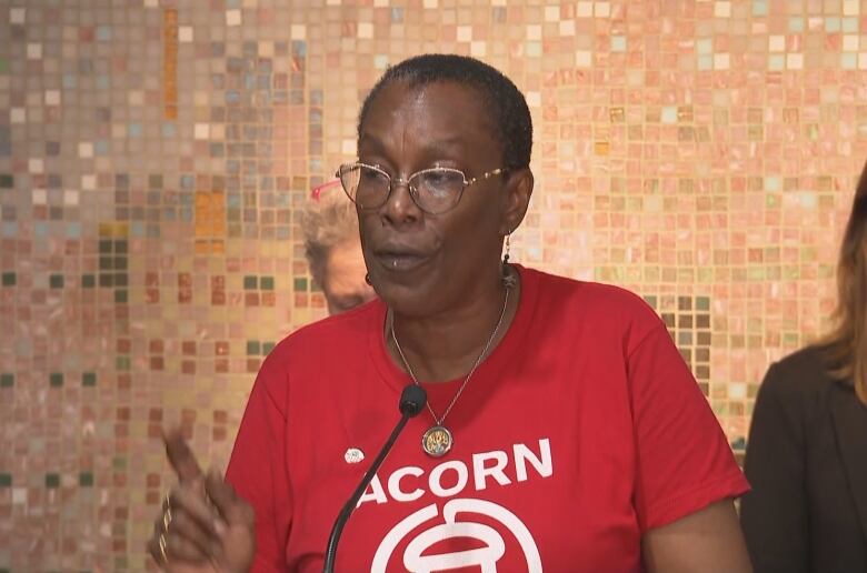 Woman in a red shirt speaks at a podium.