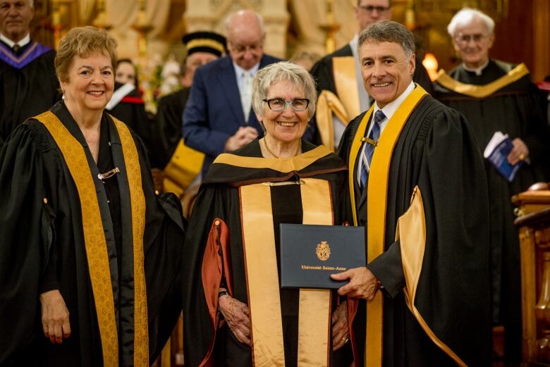 A woman wearing glasses receives an honorary degree from a university.