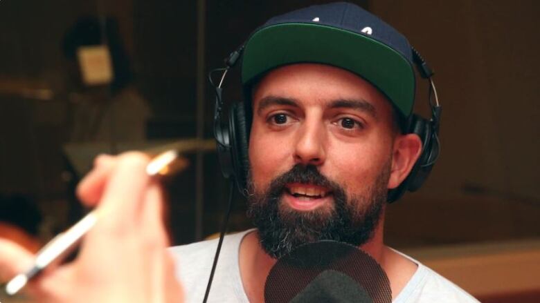 A man with dark hair and a beard is photographed while he is interviewed by a journalist.