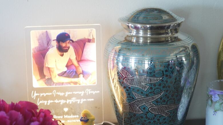 A condolence card with a man's picture on it sits beside a funerary urn.