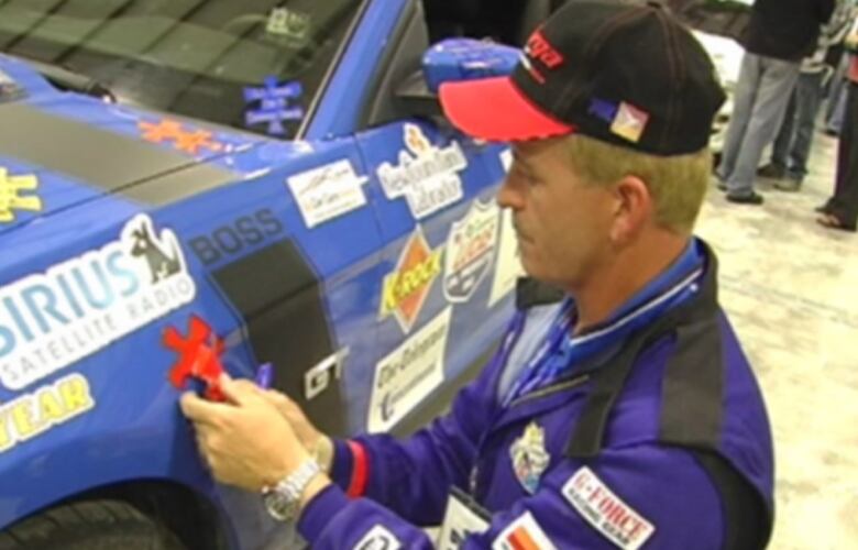 A man in a blue jumpsuit is putting a sticker on the side of a car. 