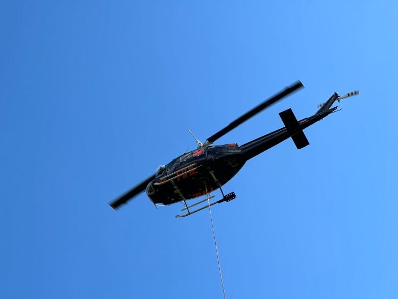 A black helicopter with a rope under it.