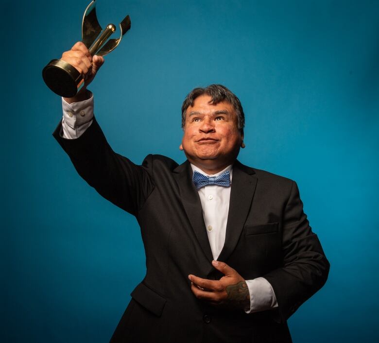 A man in tuxedo holds an award high up above his head