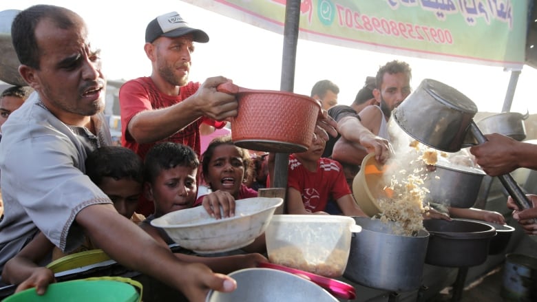 Hungry Palestinians jostle for food with bowls in their hands.