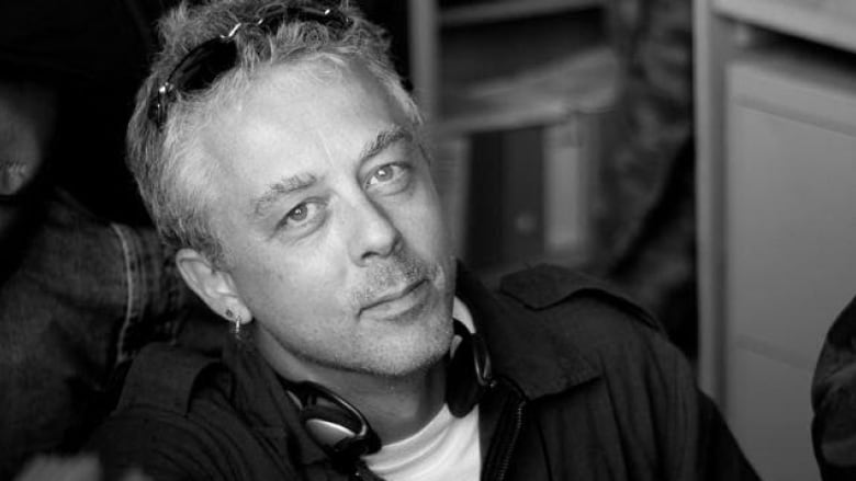 a black and white photo of a white man with grey hair and ear phones around his neck and sunglasses on his head