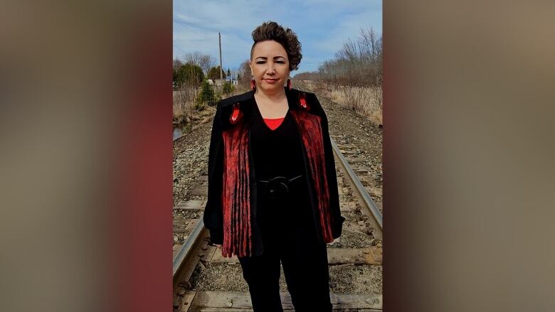 A woman dressed in black and red standing on a train track.