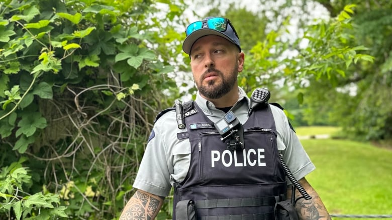 A man in a police vest stands in a green area at the Canada-U.S. border.