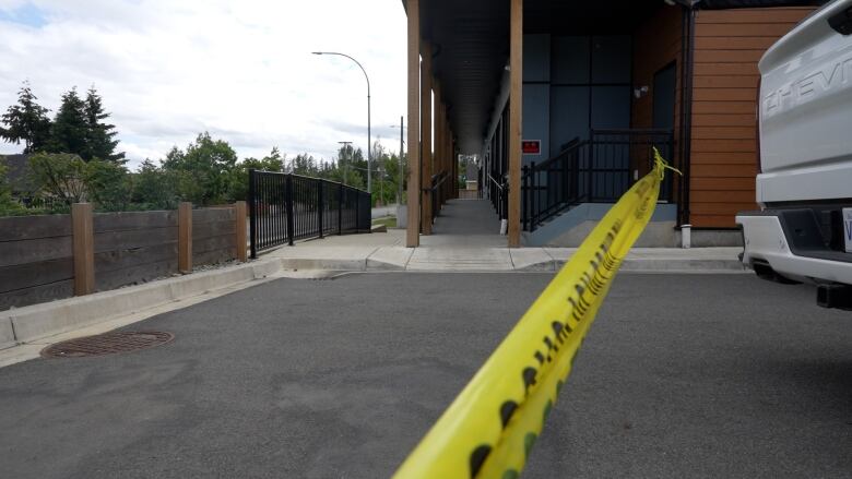 Crime scene tape separates a parking lot from a building with a ramp and a small set of stairs.