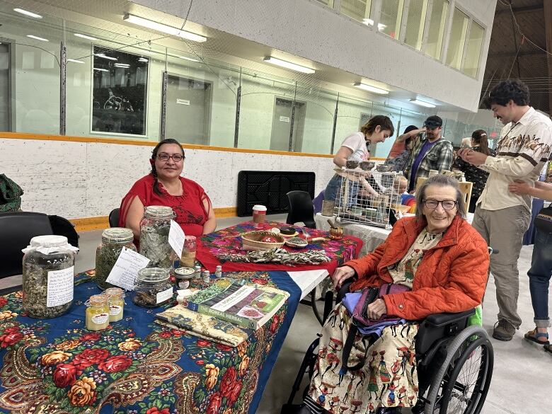 Two women sit at a table with a bright tablecloth.