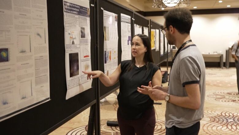 Laurie Rousseau-Nepton gestures to a poster while speaking to a man.