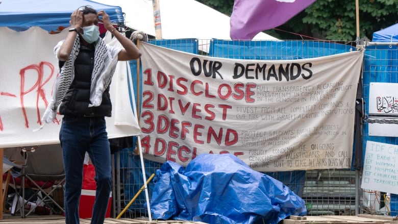 A masked man stands outside a close grouping of tents.