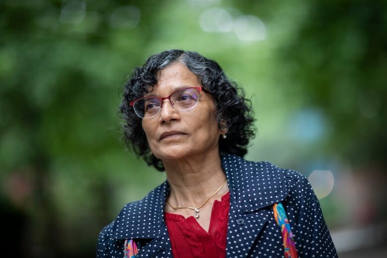 A South Asian woman wearing a black coat and a red top is pictured outdoors.