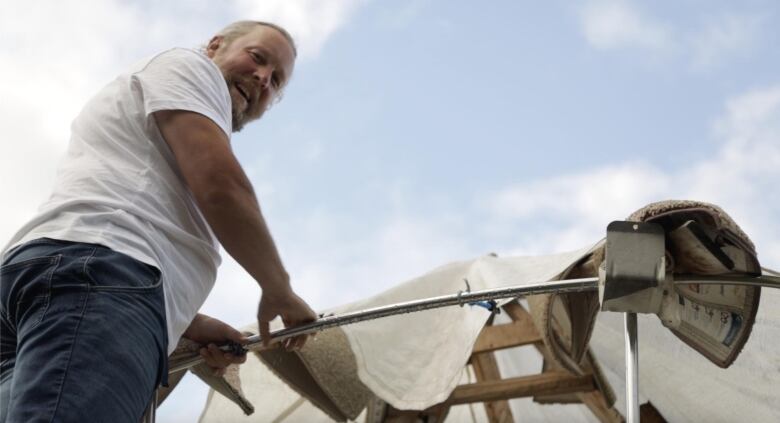 Chris Mercer, stands on a cedar ladder that rests on the stern of his boat, the Blue Lotus, looking down at the camera with a smile on his face.