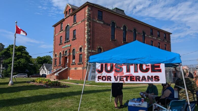 A sign saying 'Justice for veterans' in front of the Summerside courthouse against blue sky.