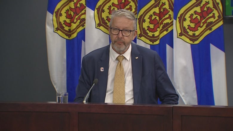 Man in suit sits at desk in front of Nova Scotia flag.