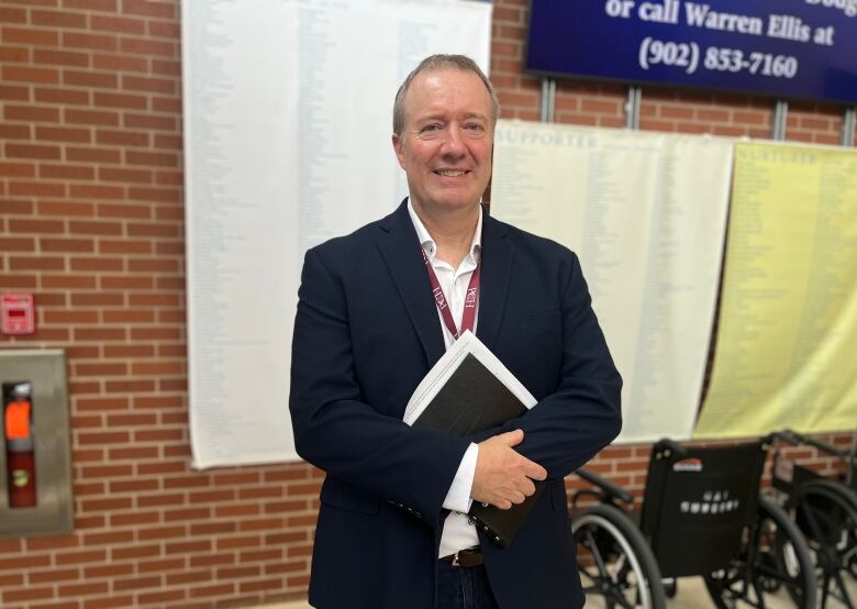 A man stands holding a book, looking at the camera. 