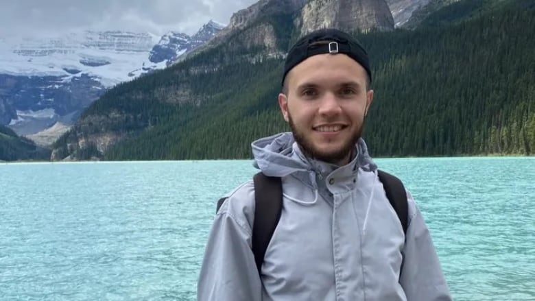 A young man standing in front of a lake.