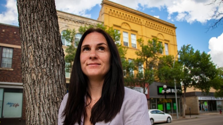 A woman stands by a tree looking up.