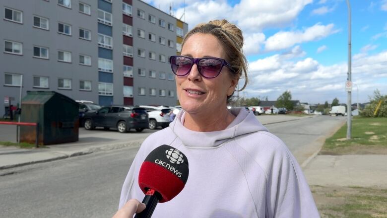 Woman with hair pulled up, wearing sunglasses talking outdoors.