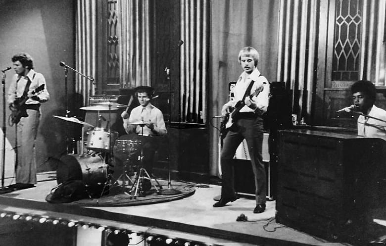 Four men perform on stage in a black and white photo.