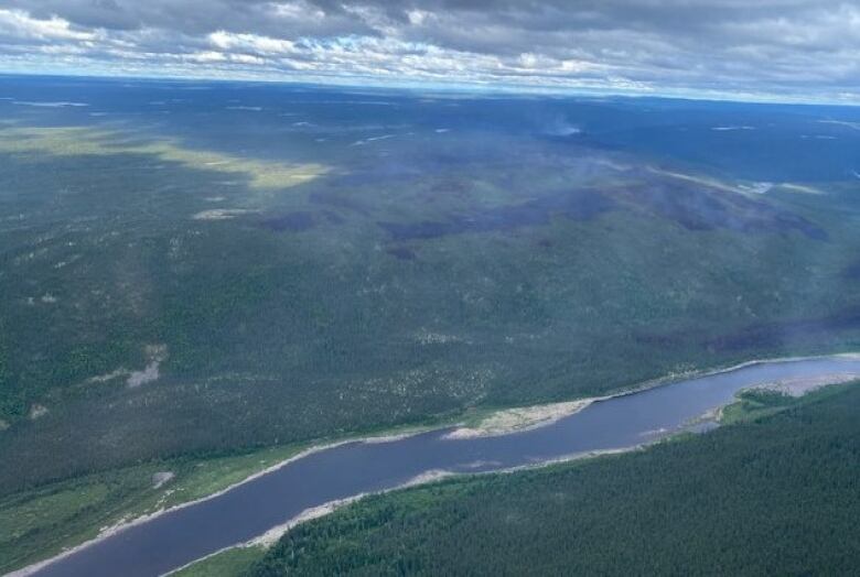 An aerial image of a river running through forested wilderness. On one side of the river there are sections of burnt and smouldering forest.