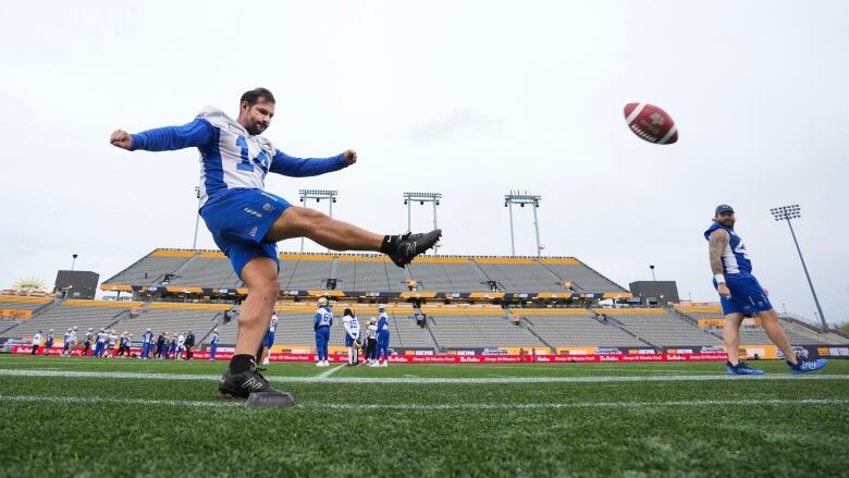 A football player wearing shorts and no helmet follows through on a placekick during practice.