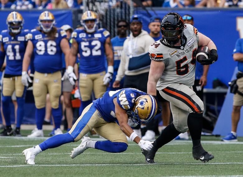 A tackler in blue reaches for the ankle of a ball-carrier in white.