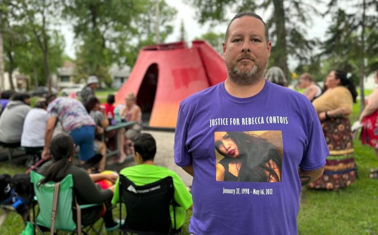 A man stands outside in front of a monument wearing a purple shirt that reads, 