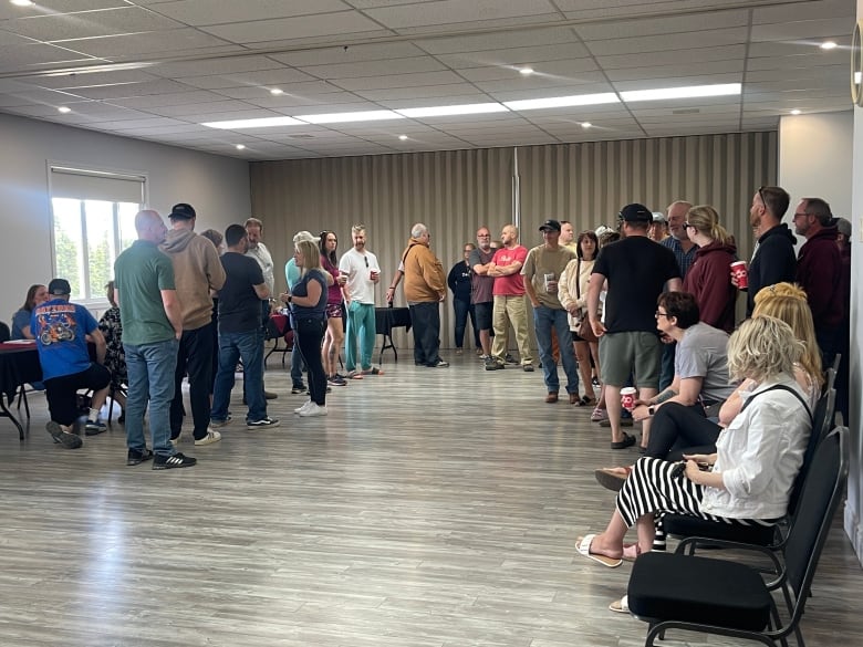 A group of around 50 people are standing in in a line inside a hotel ballroom.