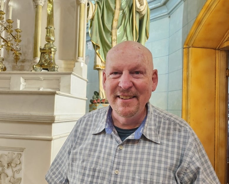 A bald-headed man in a checked blue shirt smiles for the camera.