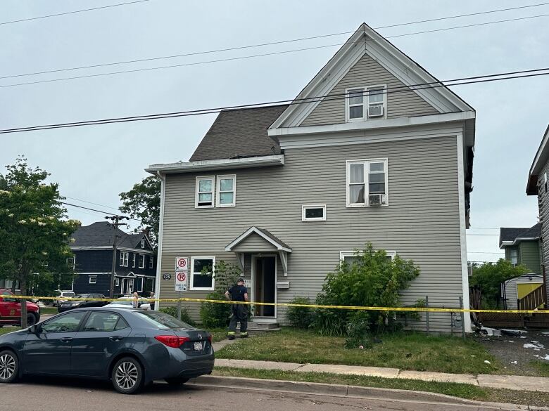 Yellow police tape stretches across the front of a grey house. 