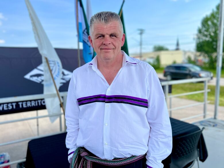 a man in a white collared shirt with a purple and black ribbon sewn across the chest and a woven metis belt