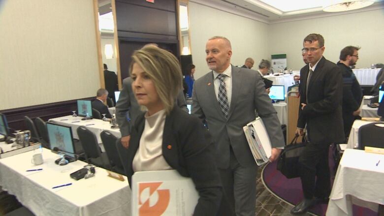 A woman with a bindert in hard walks out of a meeting room.