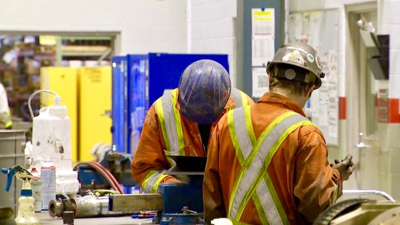 A pair of workers in overalls use equipment inside a manufacturing facility.