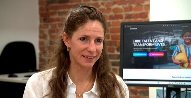 A woman is interviewed at her office with a computer monitor in the background.