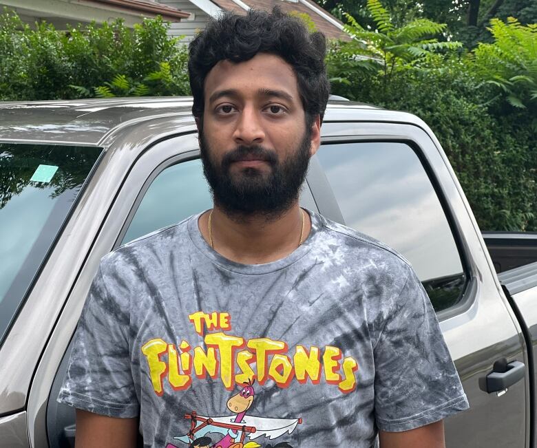 Man wearing flintstones t-shirt stands in front of truck.