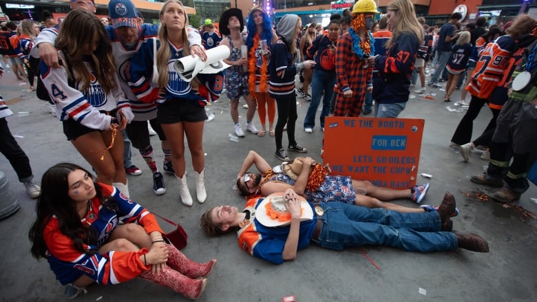 Two people lie flat on the ground as a crowd looks up sadly.