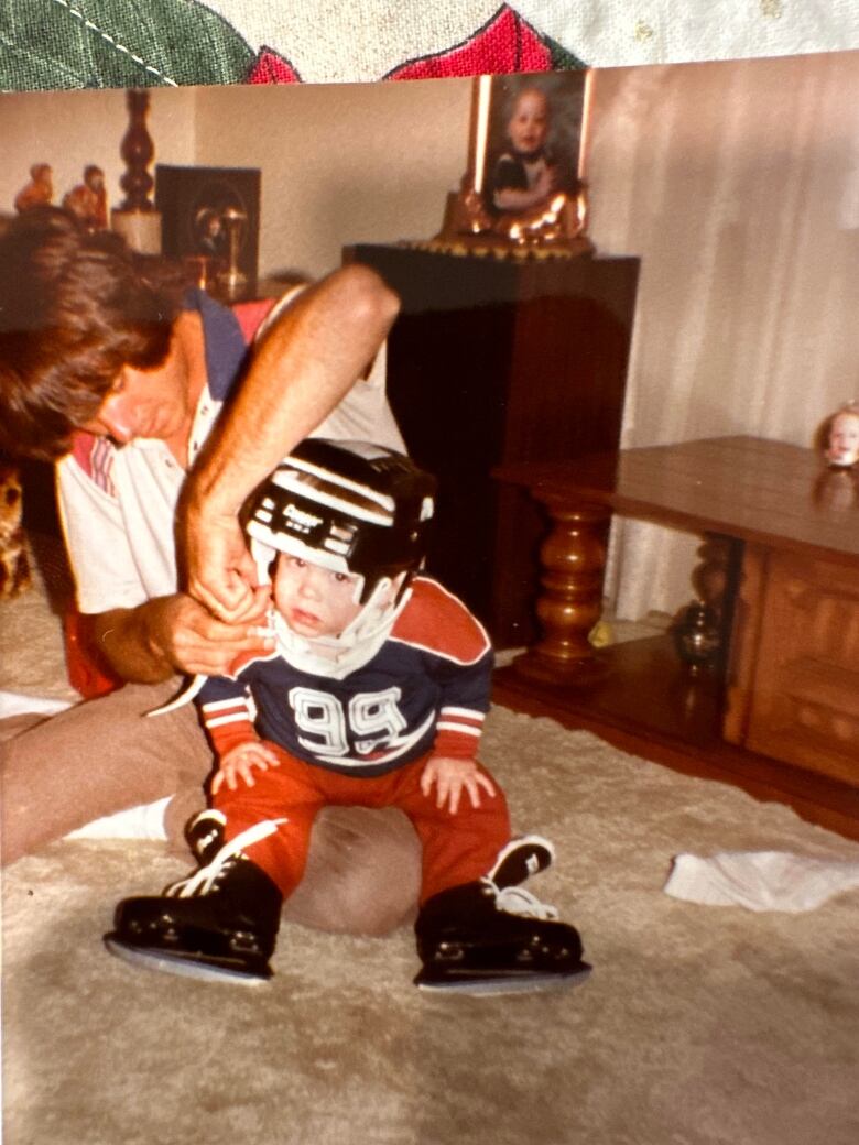 A little boy wearing an Edmonton Oilers jersey with 99 on it can be seen with a man helping fasten his helmet behind him.