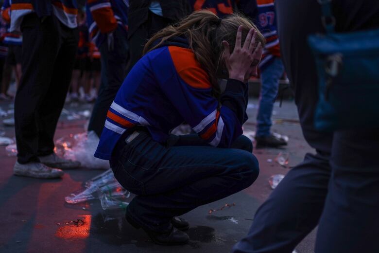 A person wearing an orange and blue jersey kneels with their face in their hands. 