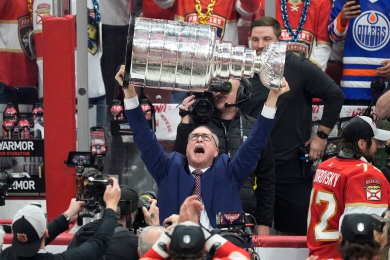 A man in a blue suit holds up a silver trophy