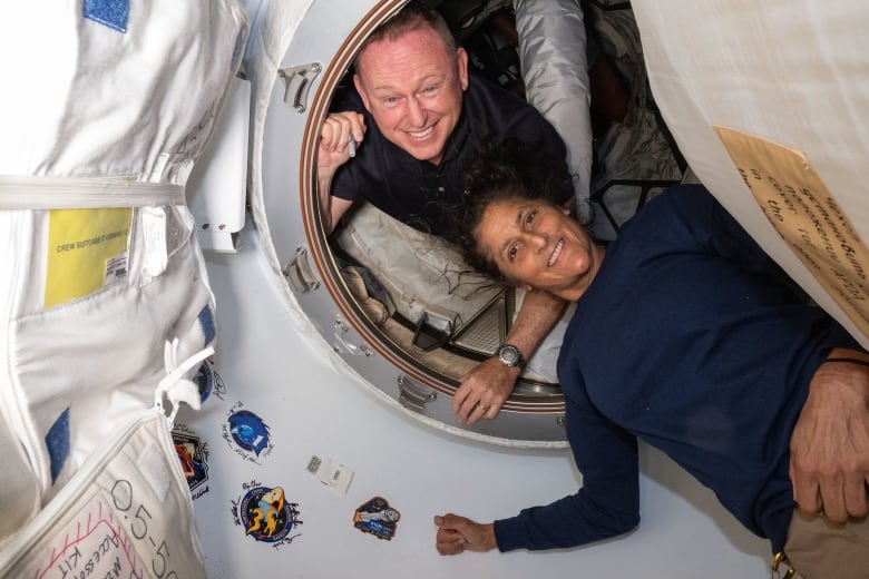 A man and a woman float in a spacecraft with big smiles.